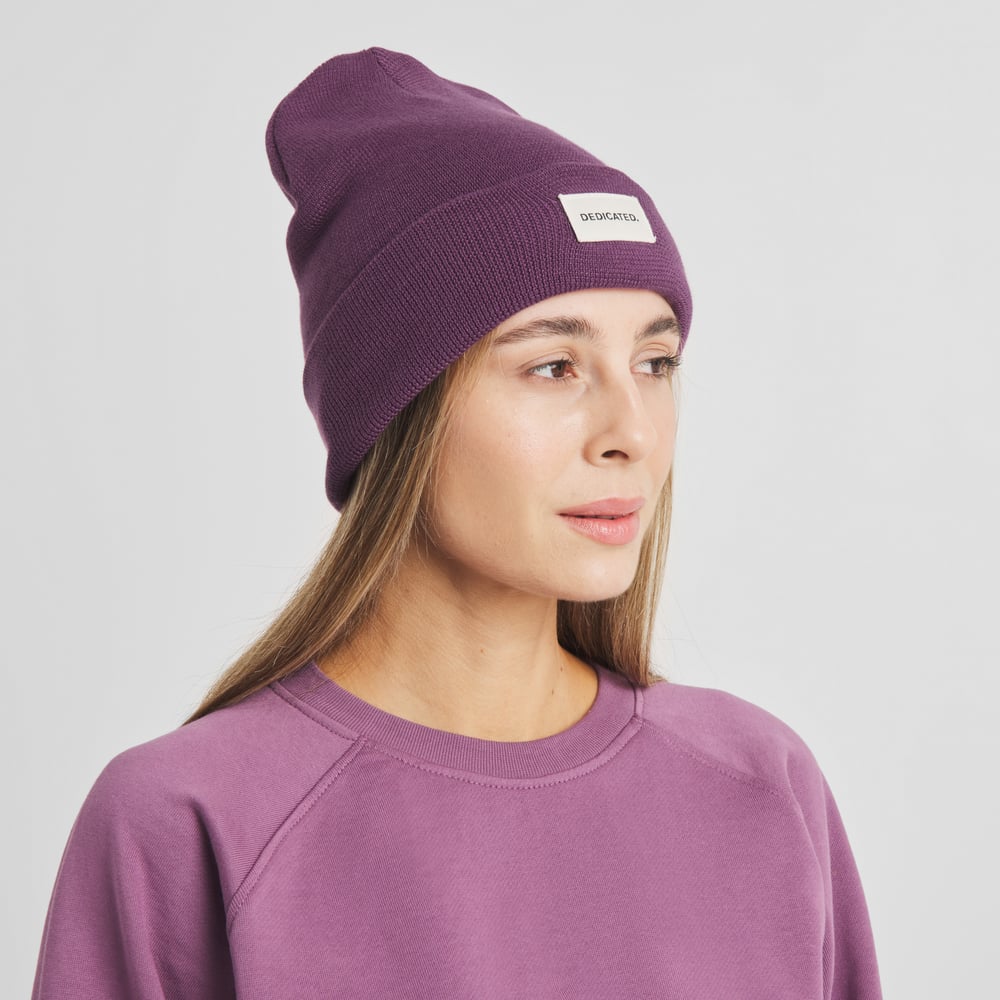 Kvinna som bär den bärlila mössan Beanie Kiruna från Dedicated och tittar åt sidan.
