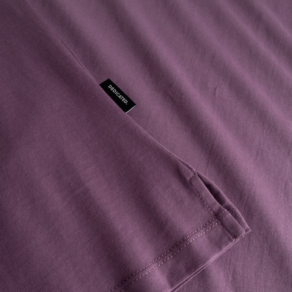 A close-up of the berry purple T-shirt Visby, showing the folded sleeve and the small black Dedicated brand label.