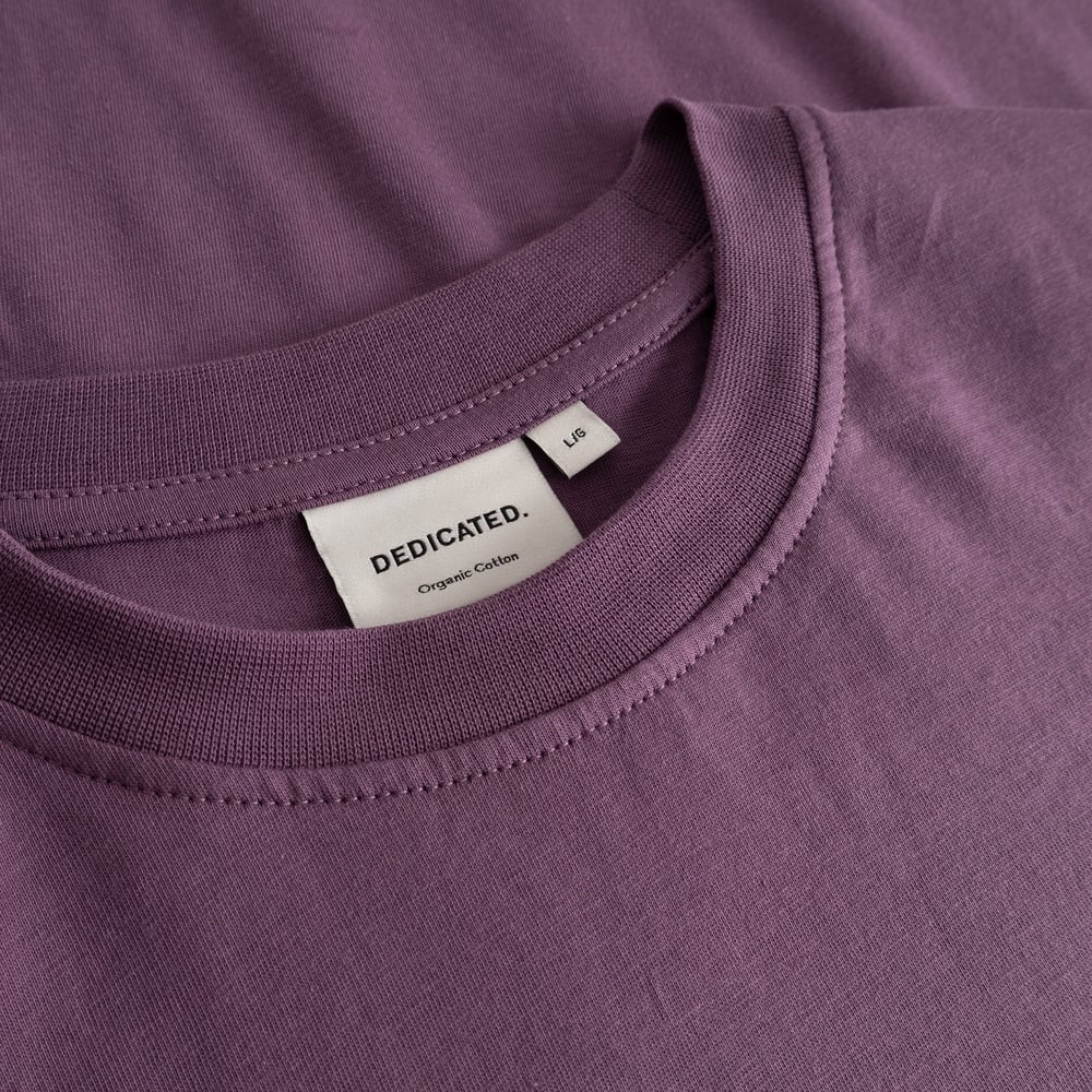 Nahaufnahme des Rippkragens und des Dedicated-Etiketts am T-Shirt Stockholm in Berry Purple aus Bio-Baumwolle.