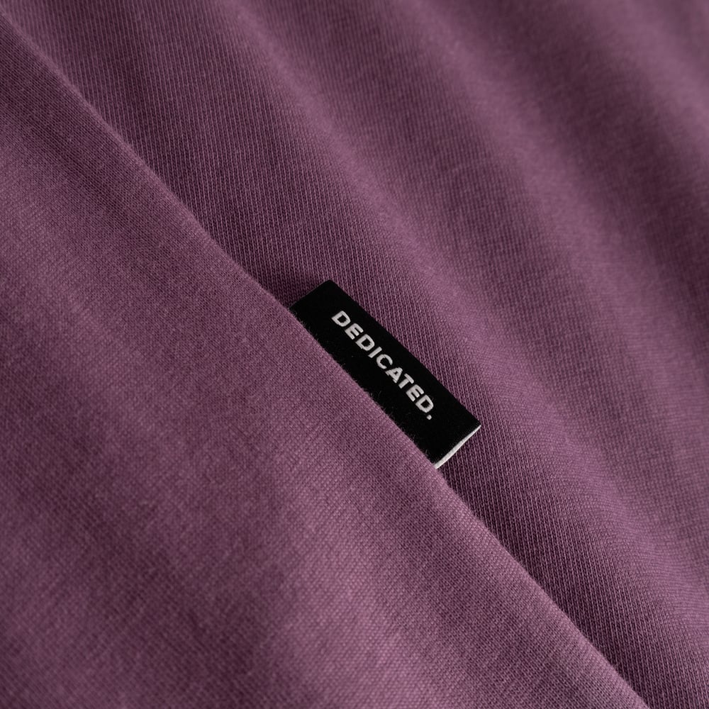 Närbild på T-shirt Stockholm Base i Berry Purple, som visar tygstrukturen och den lilla Dedicated-etiketten.