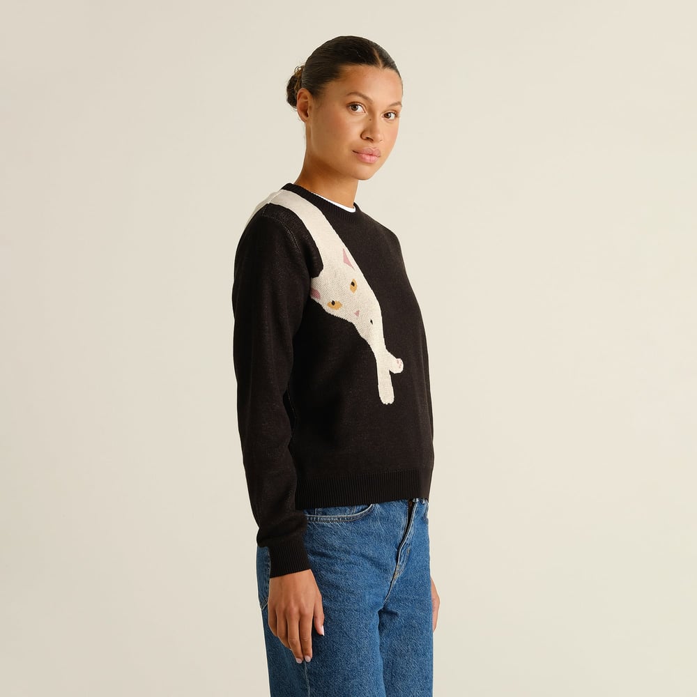 Side profile of a woman wearing the black Arendal sweater with a quirky long cat graphic, paired with blue jeans.
