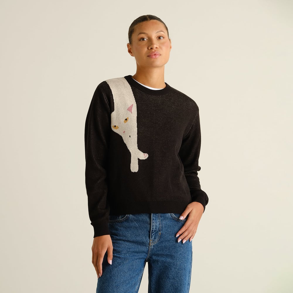 A woman models the black Arendal sweater featuring a playful long cat graphic, styled with classic blue jeans.