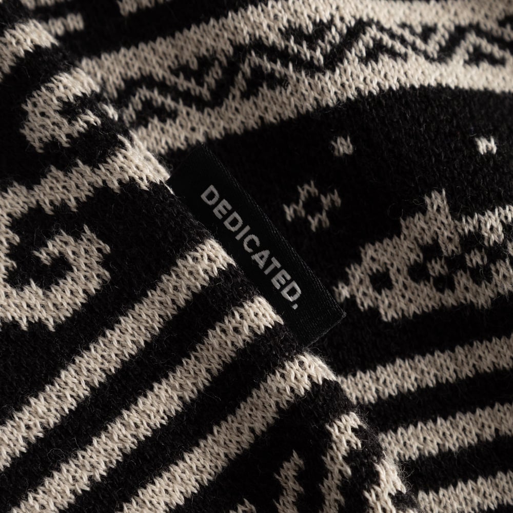 Close-up of the black and cream Fair Isle pattern on the Sweater Mora, showing the cozy knit texture and Dedicated logo tab.