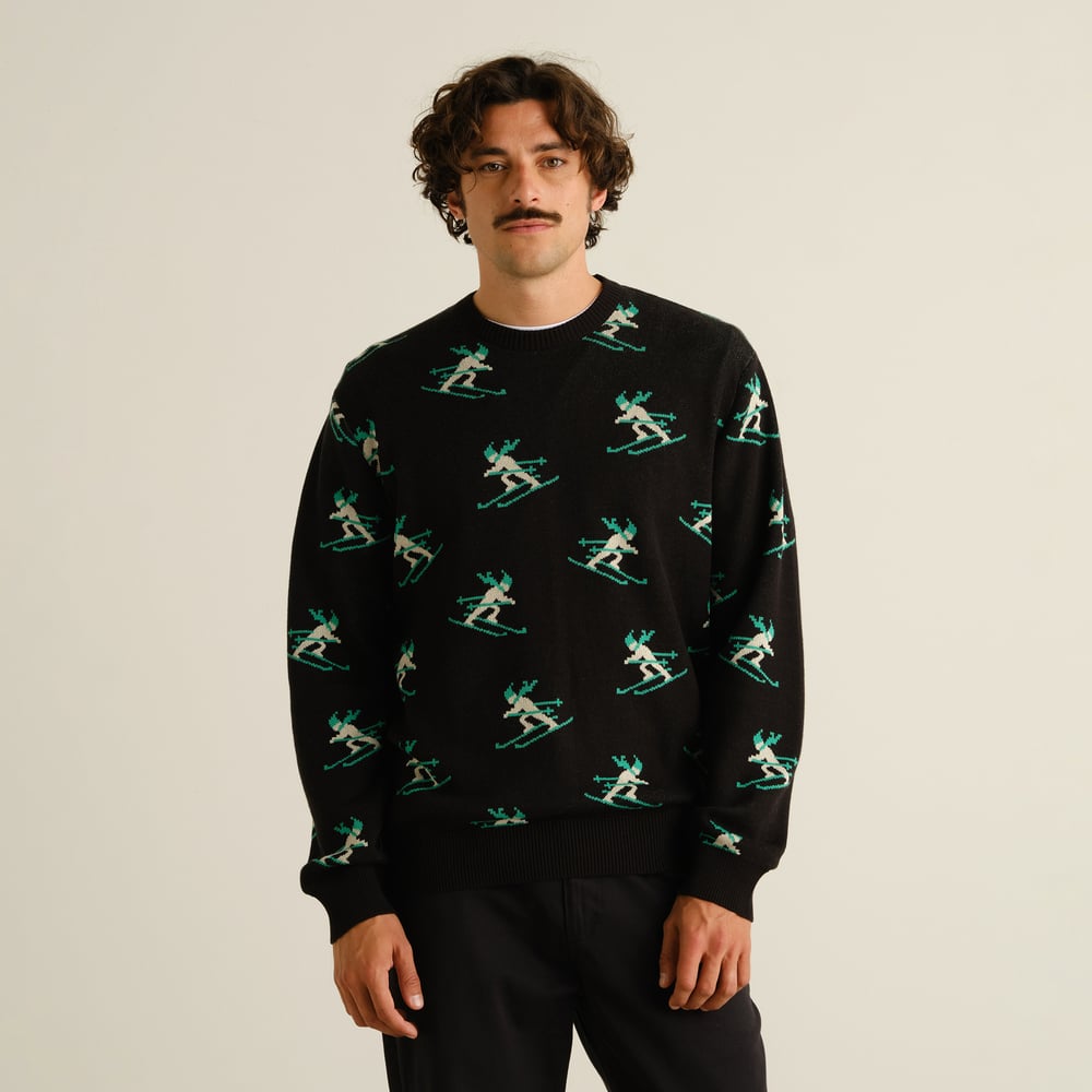 En modell med mörkt lockigt hår och mustasch bär den svarta tröjan Mora Ditsy Skier mot en ljus studiobakgrund.