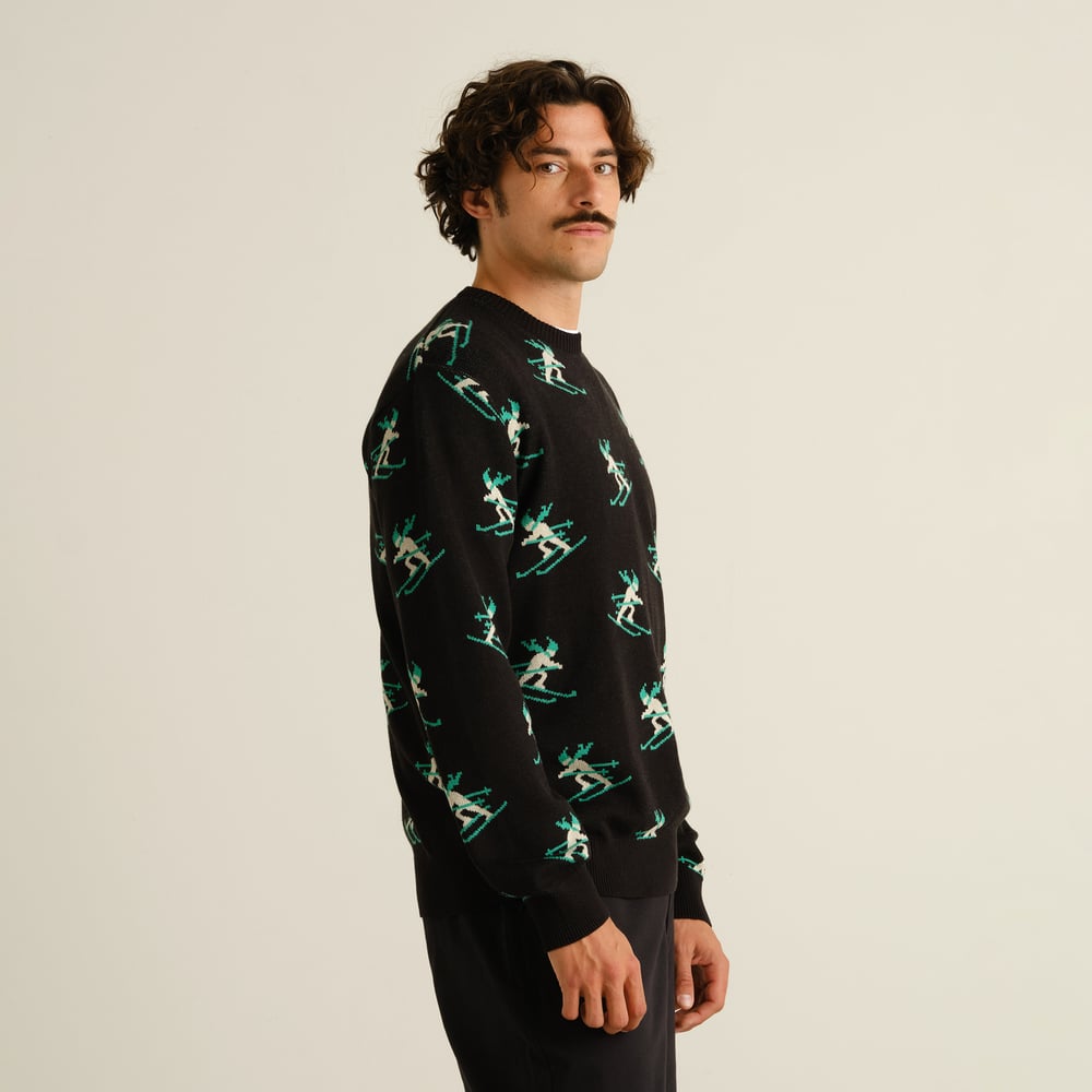 Man i profil som bär den svarta tröjan Sweater Mora Ditsy Skier med ett lekfullt, heltäckande skidåkarmönster.