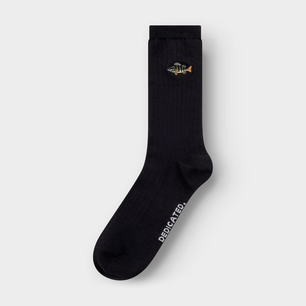 Close-up of the black ribbed Knivsta sock, featuring a detailed embroidered perch swimming by the ankle.