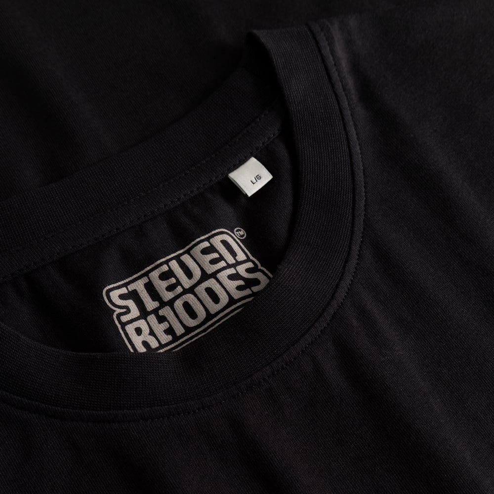 A detailed close-up of the ribbed neckline and Steven Rhodes collaboration label on the black Worship Coffee t-shirt.