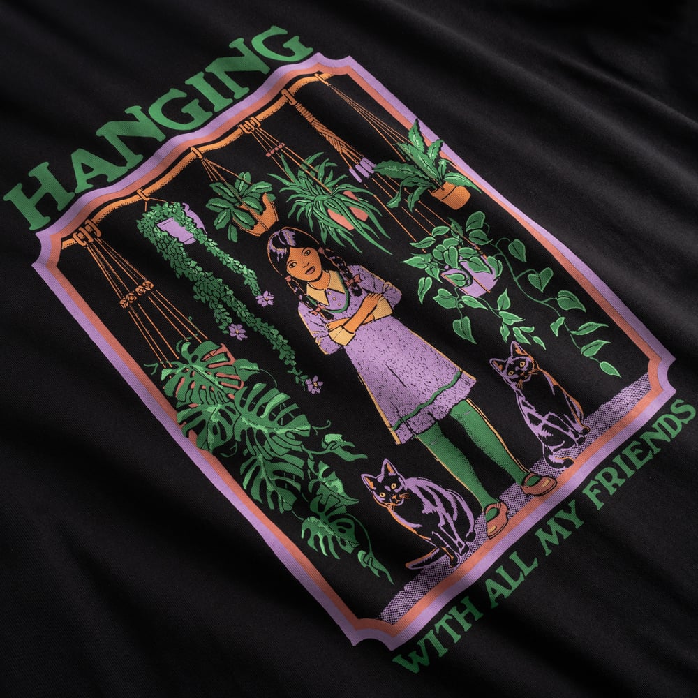 Close-up of the quirky 'Hanging With All My Friends' print, featuring a girl with her cats and plants, on a black t-shirt.