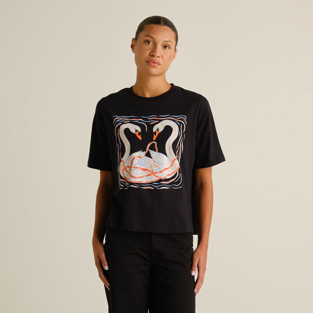 Model seen from the front wearing the black T-shirt Vadstena with a colourful painted swans graphic.