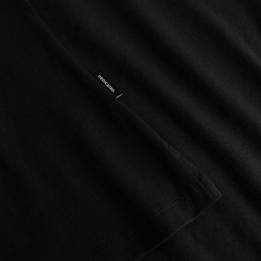 A detailed close-up of the black Visby Painted Bird T-shirt, highlighting the sleeve's texture and the classic Dedicated tag.