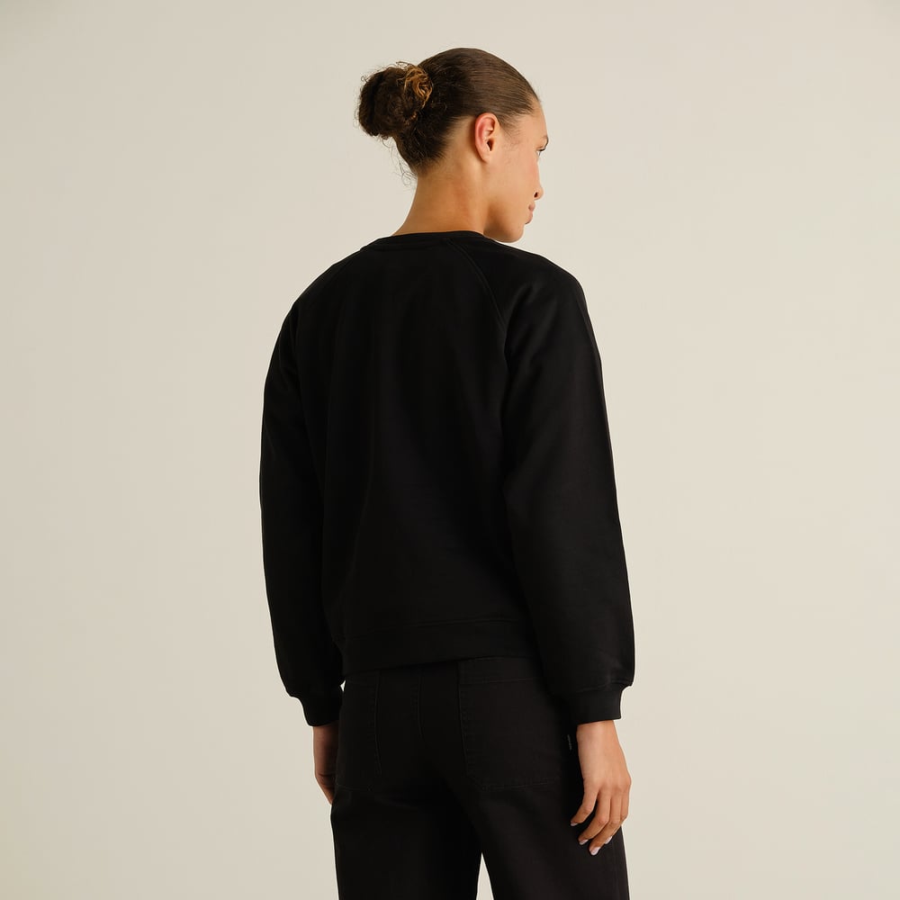 A model wearing the black Sweatshirt Ystad Painted Swans, seen from the back to showcase the fit and raglan sleeves.