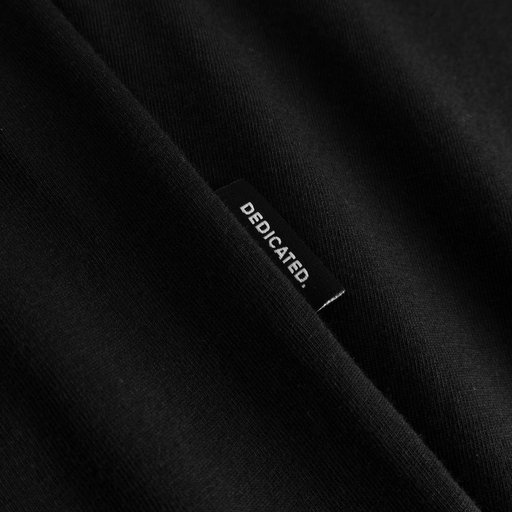 Close-up of the Dedicated brand label on the side seam of the black T-shirt Stockholm Apres Ski Instructor.