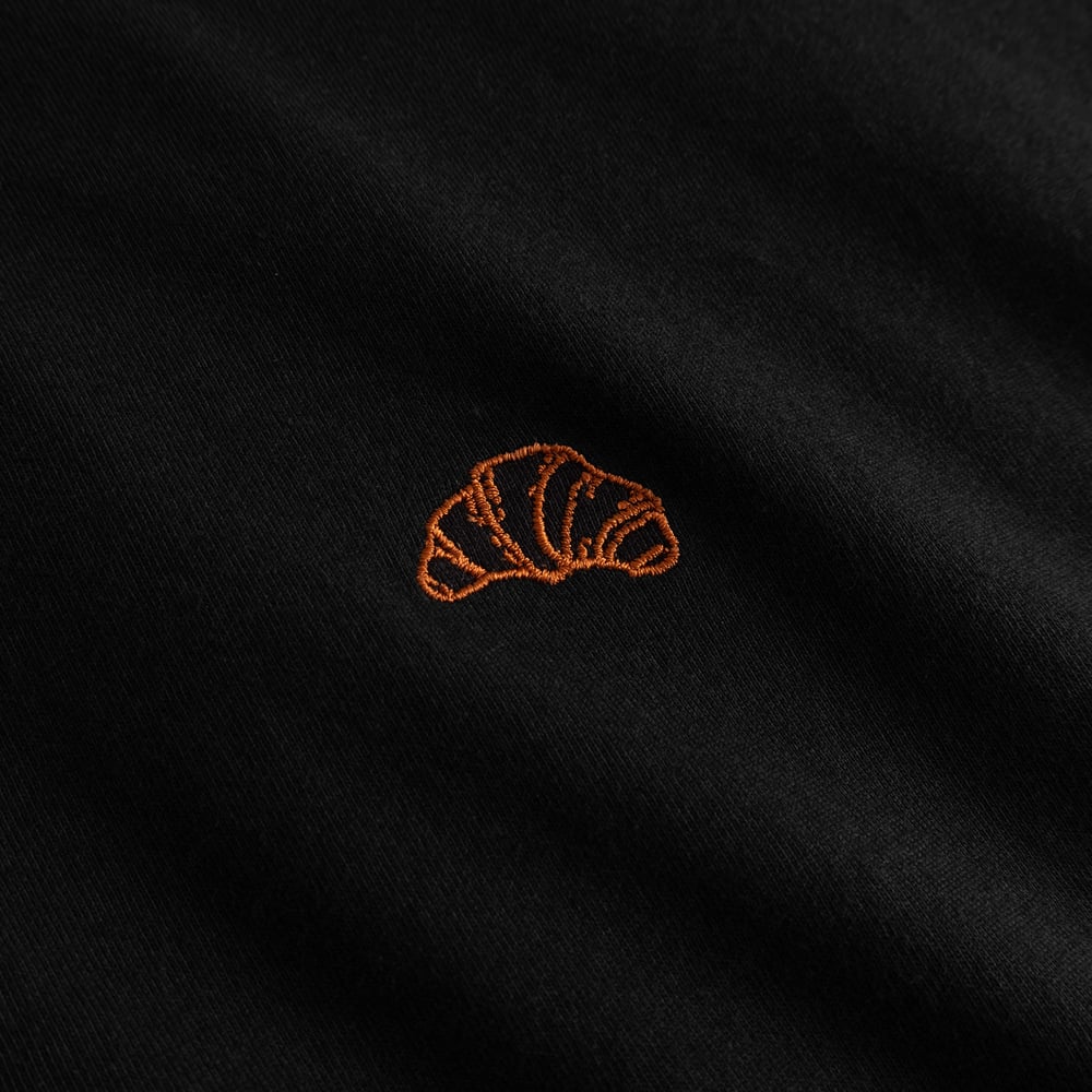 Close-up of the golden-brown croissant embroidery on the chest of the black T-shirt Visby.