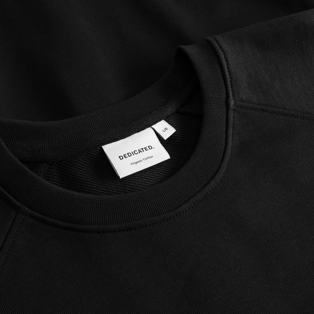 A close-up of the DEDICATED. brand label and ribbed neckline of the black Sweatshirt Malmoe Perch EMB.