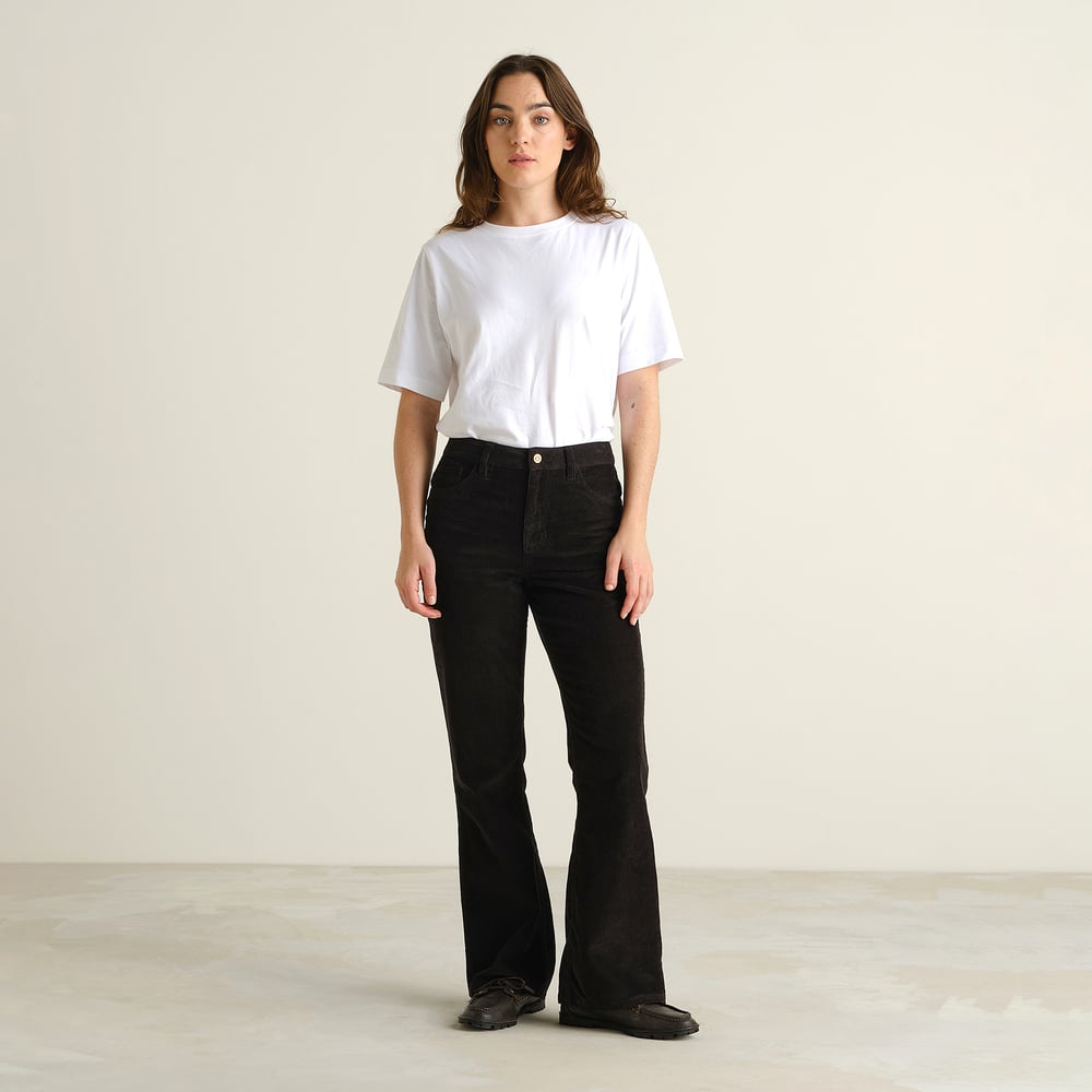 Model in Frontalansicht trägt die schwarze Cordhose Ryda im Bootcut-Stil zu einem weißen T-Shirt.