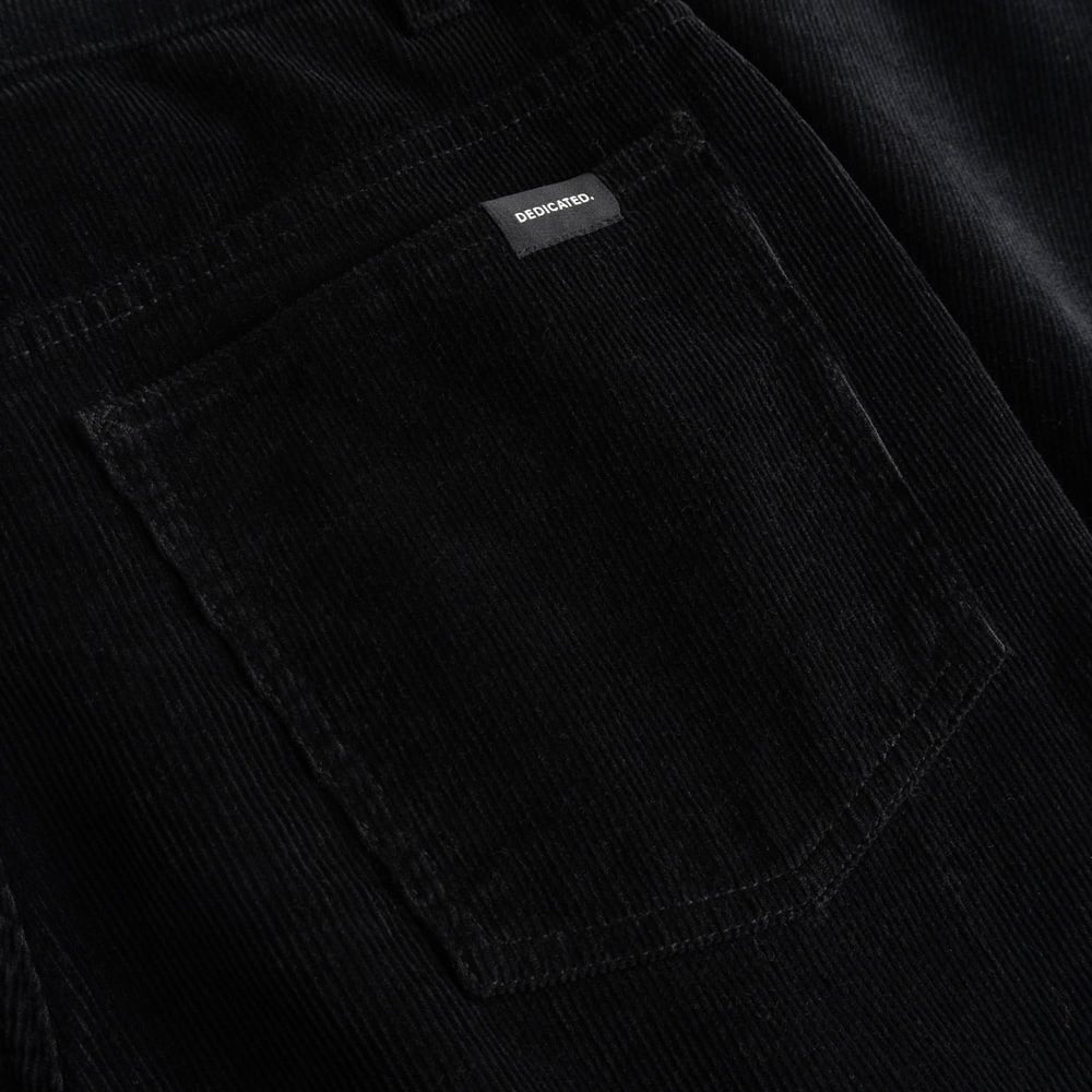 Nahaufnahme der Gesäßtasche der schwarzen Cordhose Ryda. Zu sehen sind die Cordstruktur und das kleine Dedicated-Markenlabel.