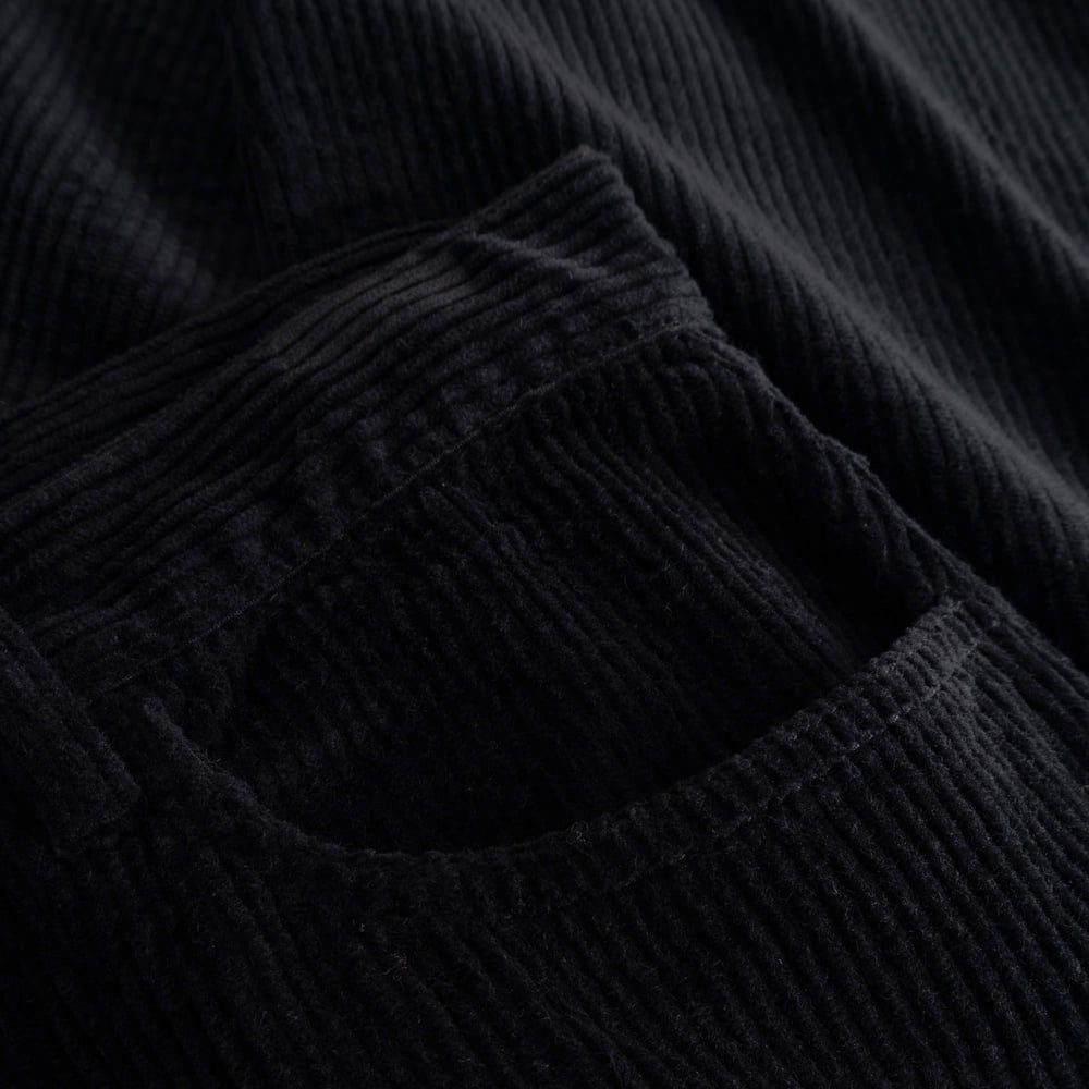A close-up view of the rich, ribbed corduroy fabric and front pocket of the black Hamburg pants.