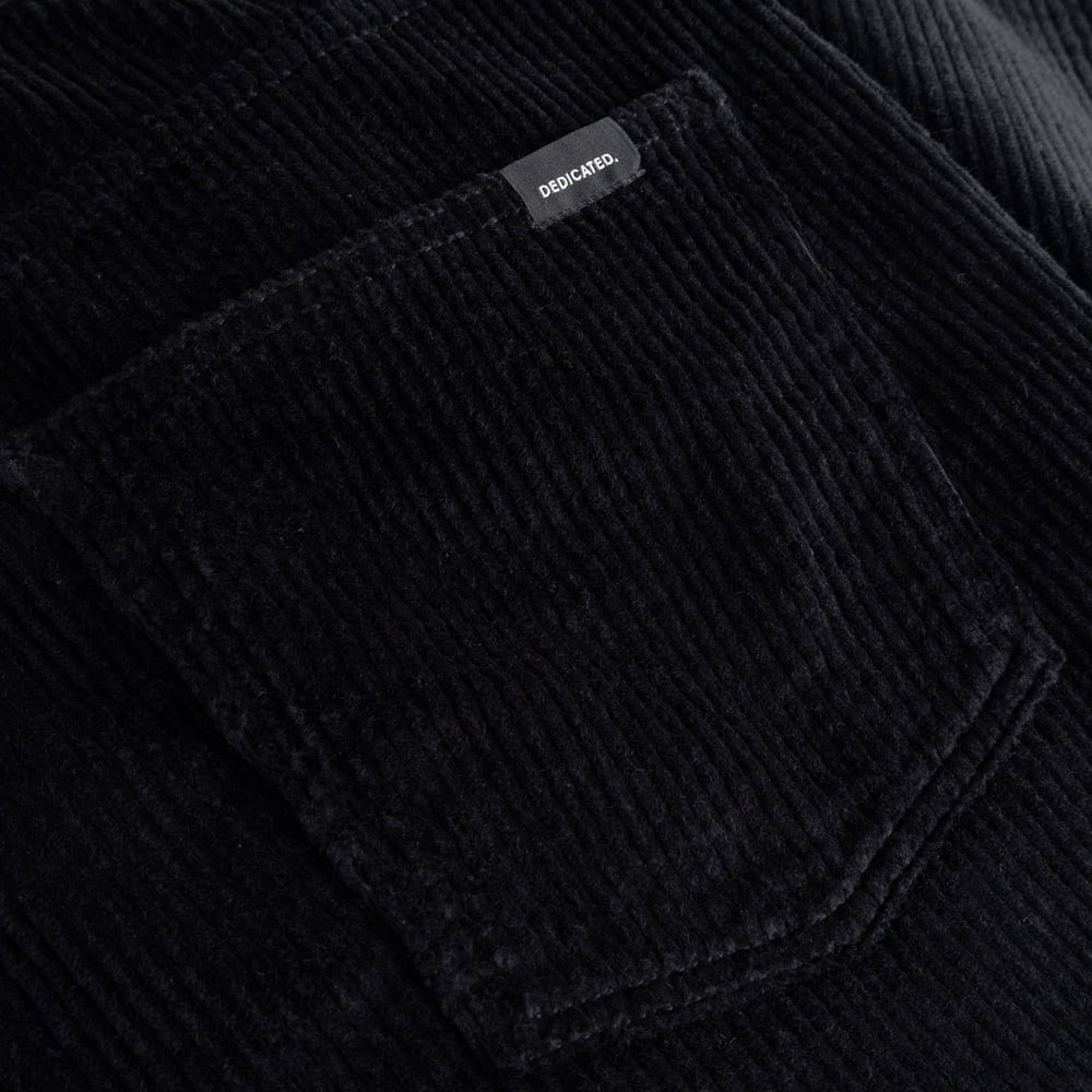 A close-up shot of the rich black corduroy fabric and back pocket of the Hamburg pants, showing the Dedicated brand label.
