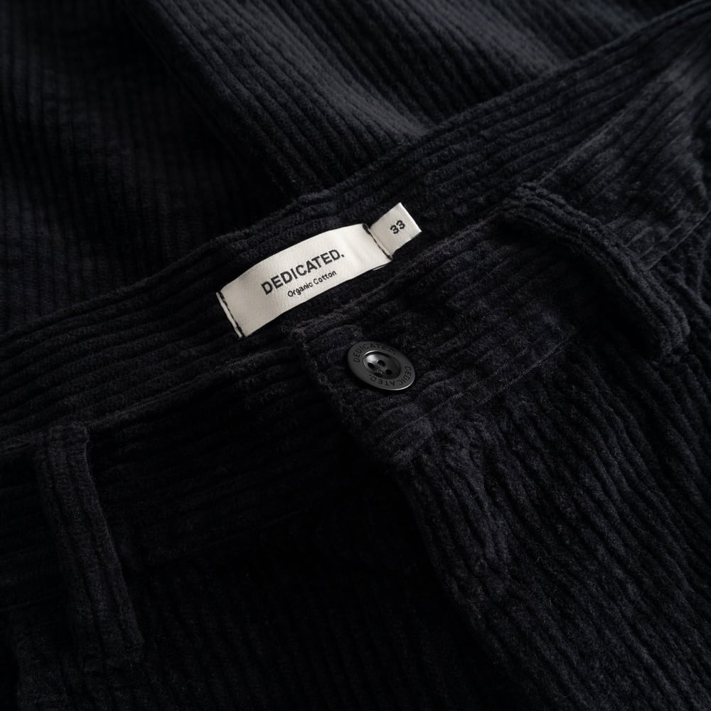 Close-up of the waistband on the black Hamburg Corduroy Pants, showing the Dedicated brand label and button detail.