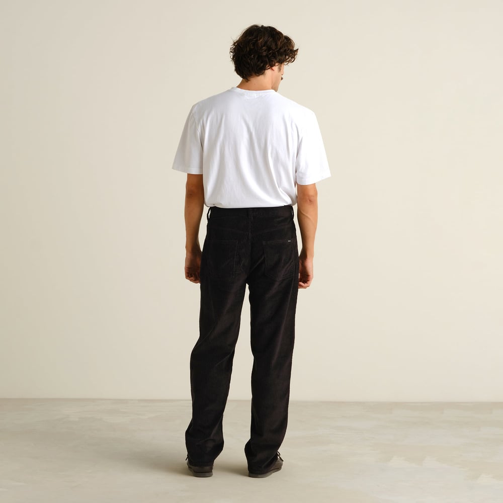 Back view of a model wearing the relaxed-fit Hamburg Corduroy Pants in black with a white t-shirt.