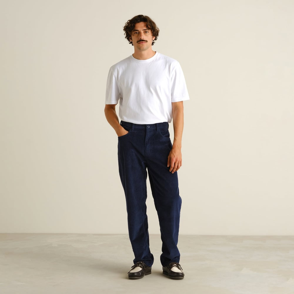 Full-length shot of a model wearing the relaxed-fit Hamburg Corduroy Pants in navy with a classic white t-shirt.
