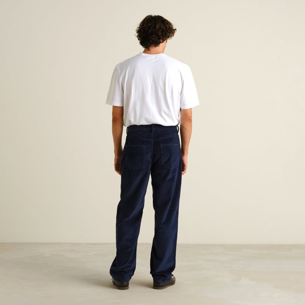 Man seen from behind wearing the relaxed-fit Hamburg Corduroy Pants in navy with a simple white tee.