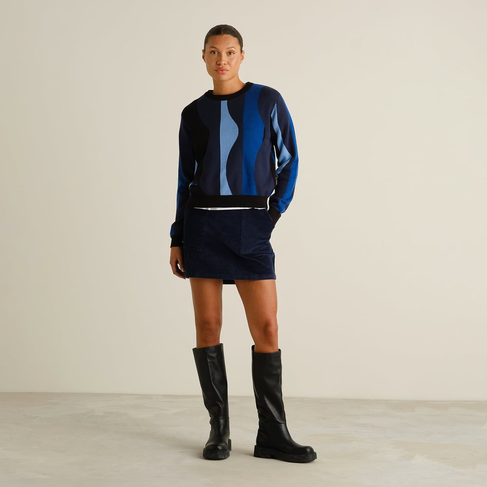 Full length view of a model wearing the Sweater Arendal Wavy Stripe Blue with a navy mini skirt and black boots.