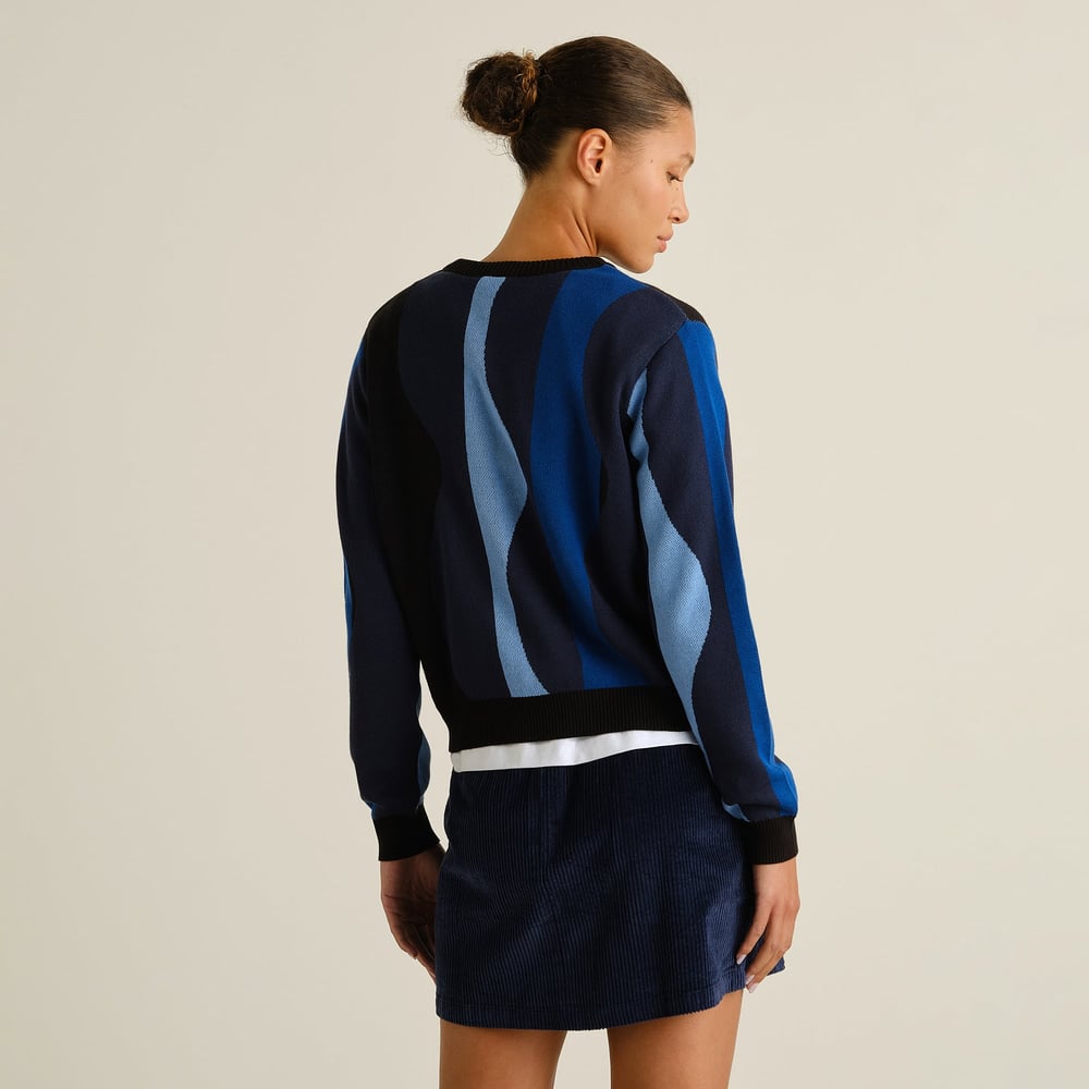 Model seen from the back wearing the Sweater Arendal with a blue wavy stripe pattern, paired with a dark blue corduroy skirt.