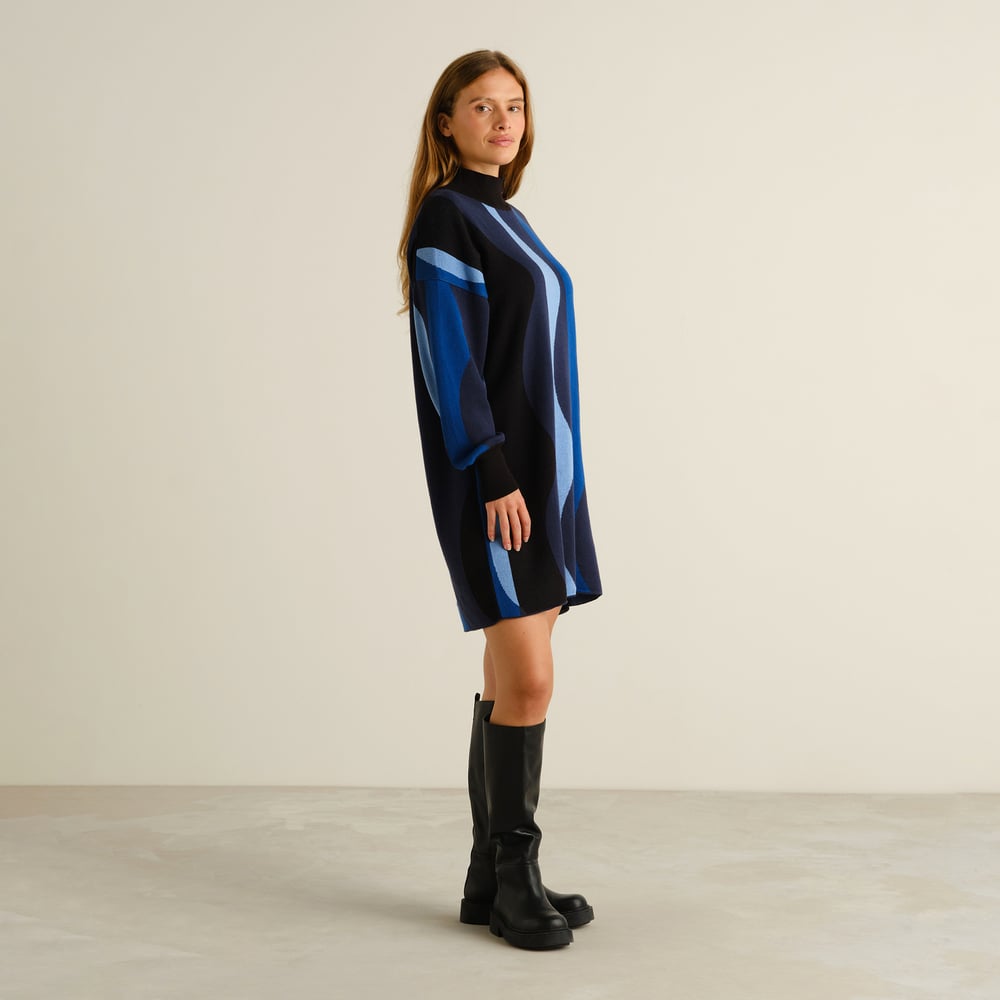 A side view of a model in the Dress Nikkala Wavy Stripe Blue, paired perfectly with black knee-high boots.