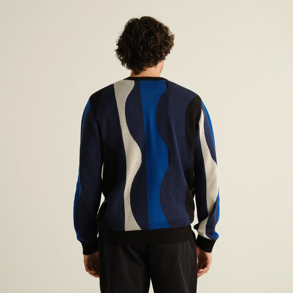 Model seen from behind wearing the Sweater Mora, showing off its cool wavy stripe pattern in blue, black, and grey.