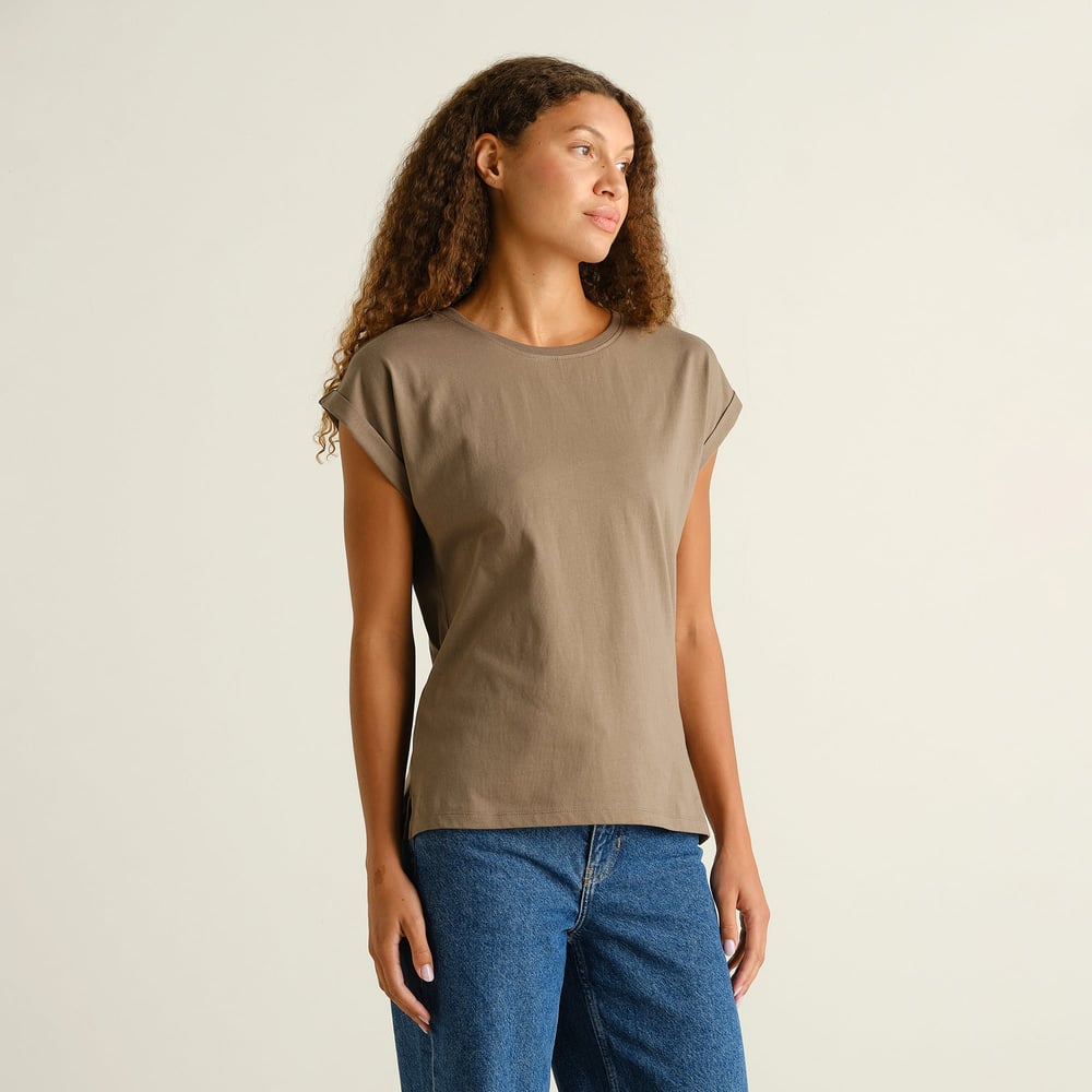 Model with curly hair wears the green Visby Base t-shirt with folded sleeves, paired with blue jeans.