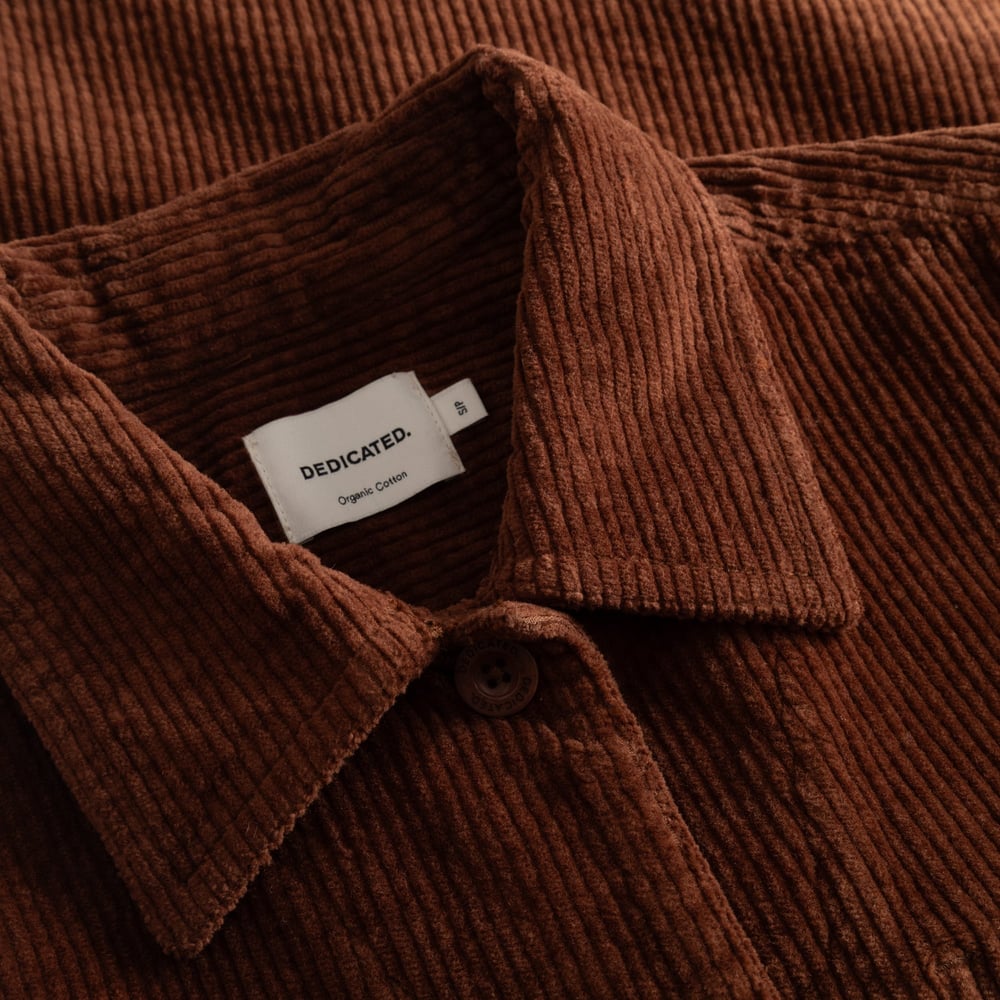 A close-up of the soft, ribbed texture of the Stiby Corduroy Jacket in Cappuccino Brown, featuring the Dedicated brand label.