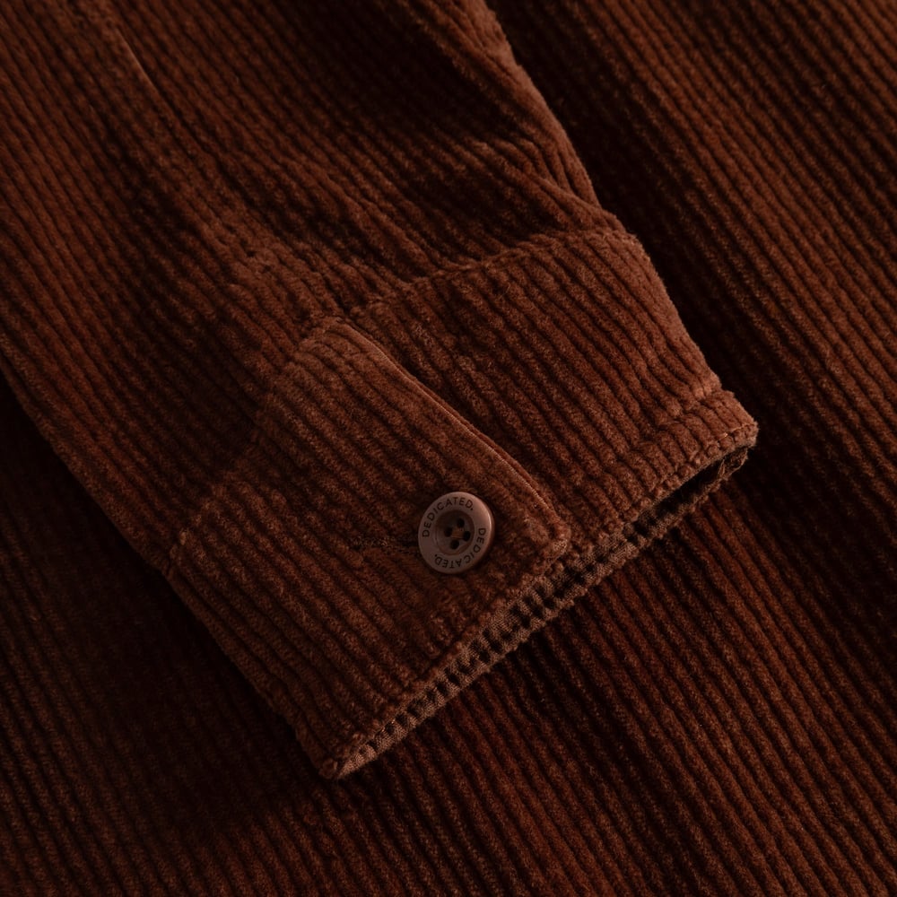 A close-up on the rich texture of the Stiby Corduroy Jacket in cappuccino brown, focusing on the buttoned sleeve cuff.