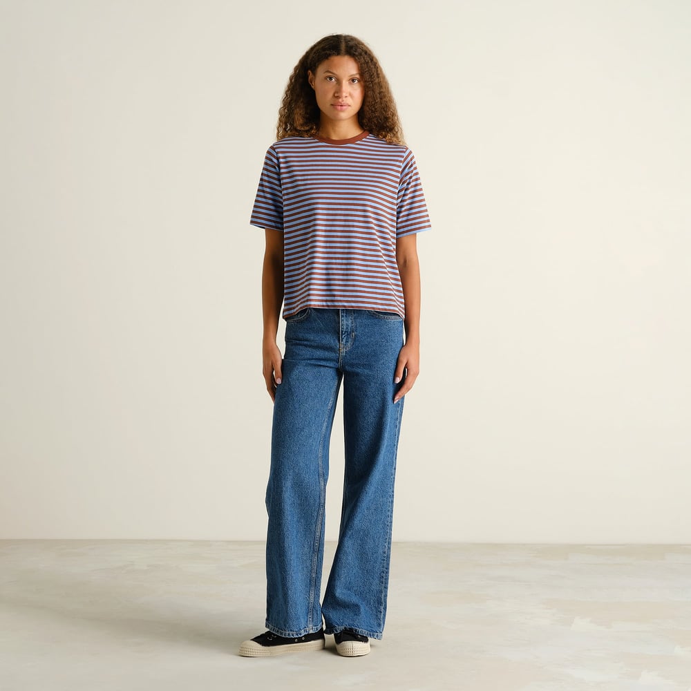 A woman with curly hair looks cool and casual in a striped tee with cappuccino brown and cornflower blue stripes and jeans.
