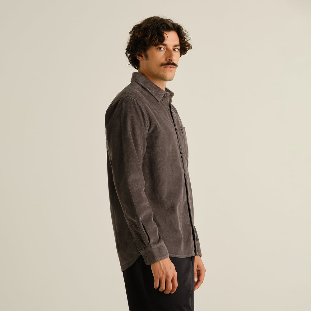 Side profile of a model wearing the Shirt Varberg Corduroy in Rock Grey, looking over his shoulder against a plain backdrop.