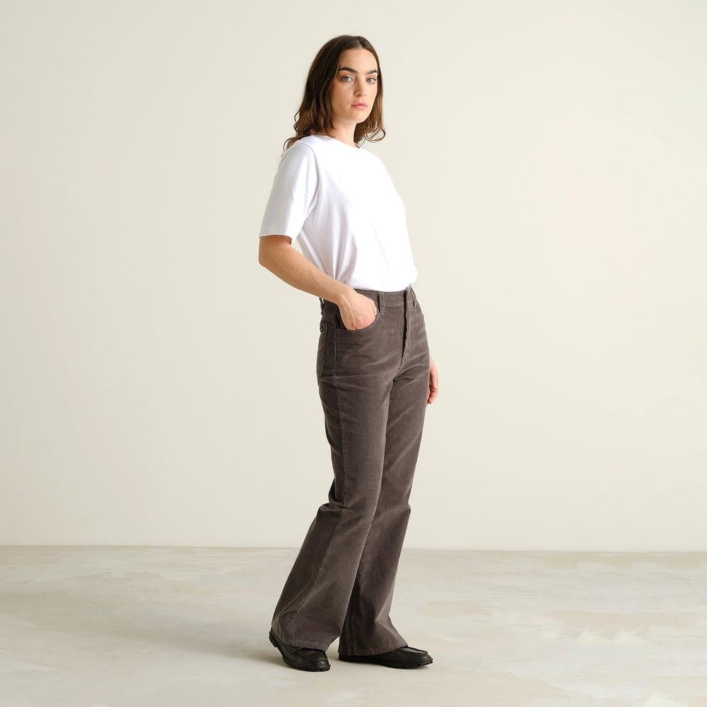 Ein Model trägt die Bootcut-Cordhose Ryda in Rock Grey und ein schlichtes weißes T-Shirt.