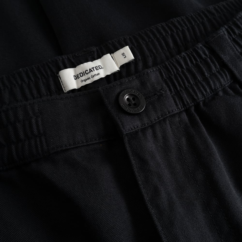 Detailed look at the black Hudiksvall Chinos, showing the comfortable elastic waistband and the Dedicated brand label.
