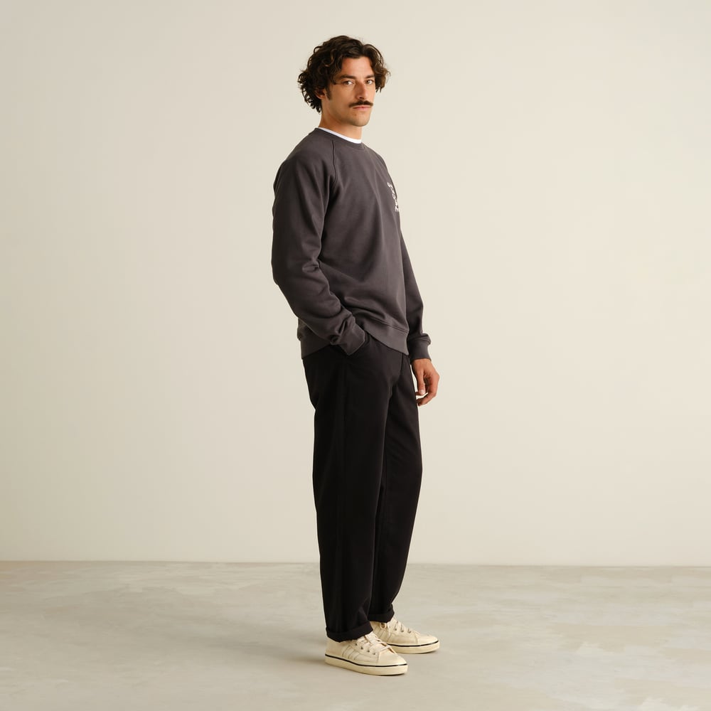 A model wears the black Chino Pants Hudiksvall, styled with a grey sweatshirt and sneakers for a relaxed, polished look.