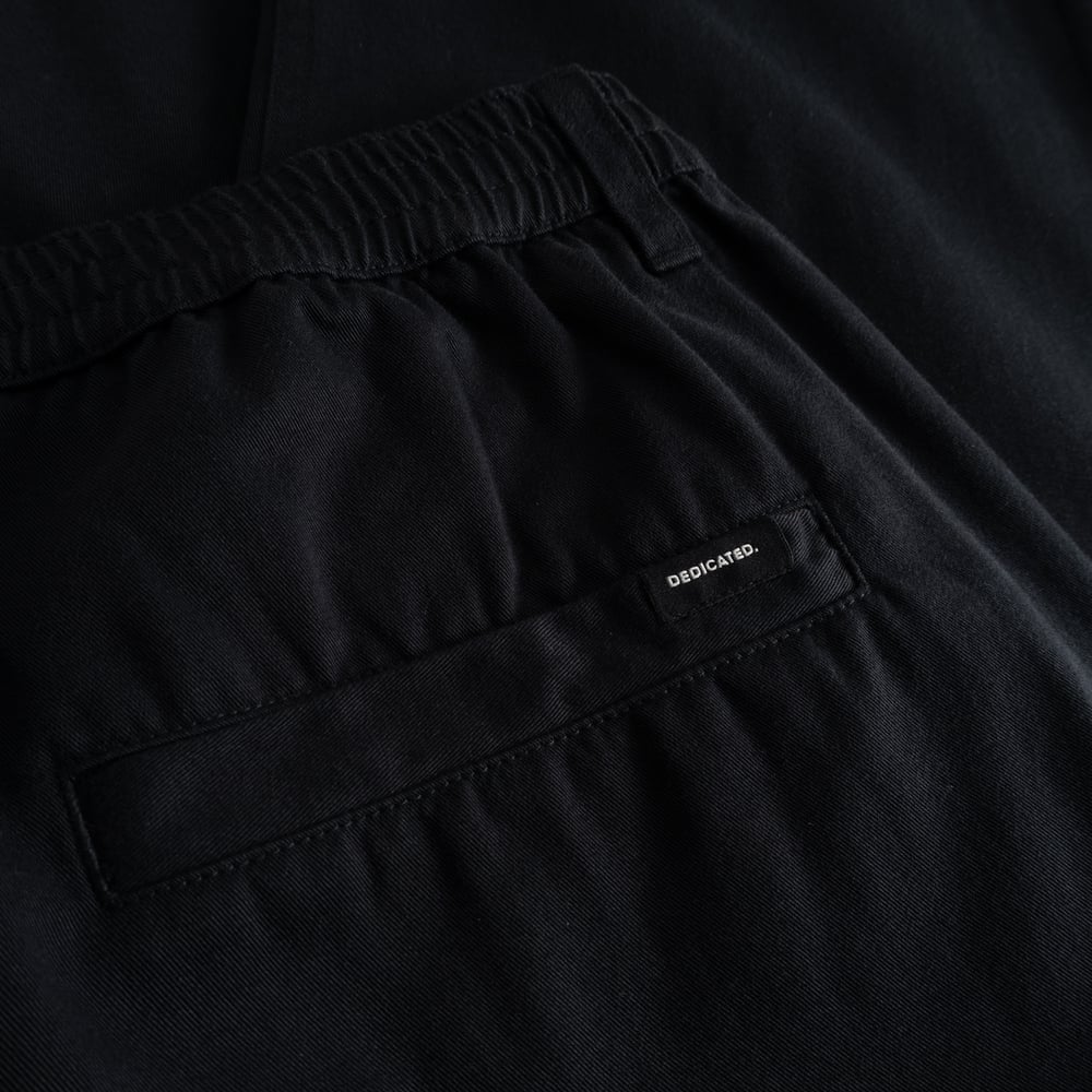 A detailed look at the comfy elastic waistband and back welt pocket of the black Hudiksvall Chino Pants.