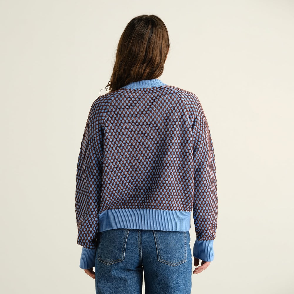 Baksidan av en kvinna som bär den stickade tröjan Husie Bubble Knit i blått och brunt med blå jeans.