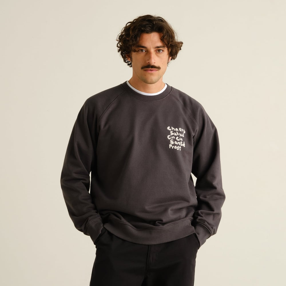 Front view of a model wearing the dark grey Sweatshirt Malmoe, with the 'Cheers Salud' graphic on the chest.