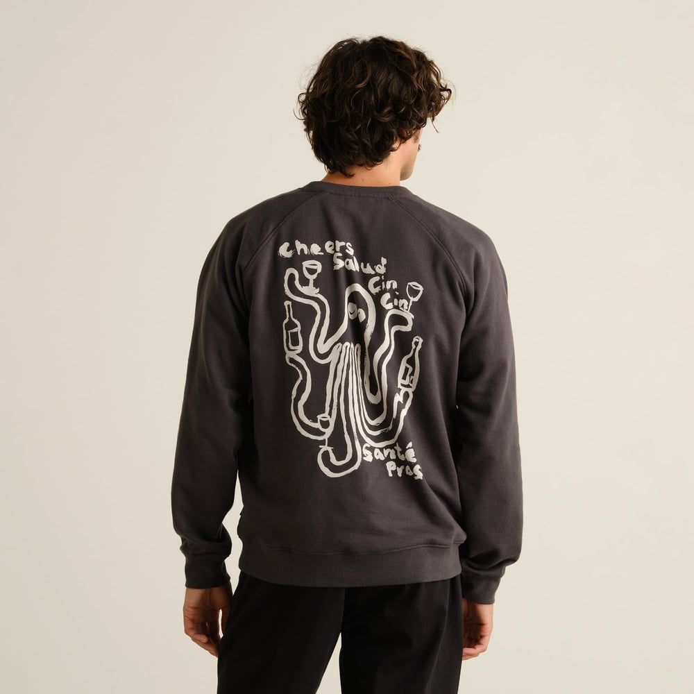Model seen from behind wearing a charcoal grey sweatshirt with a playful white graphic of an octopus toasting with wine.