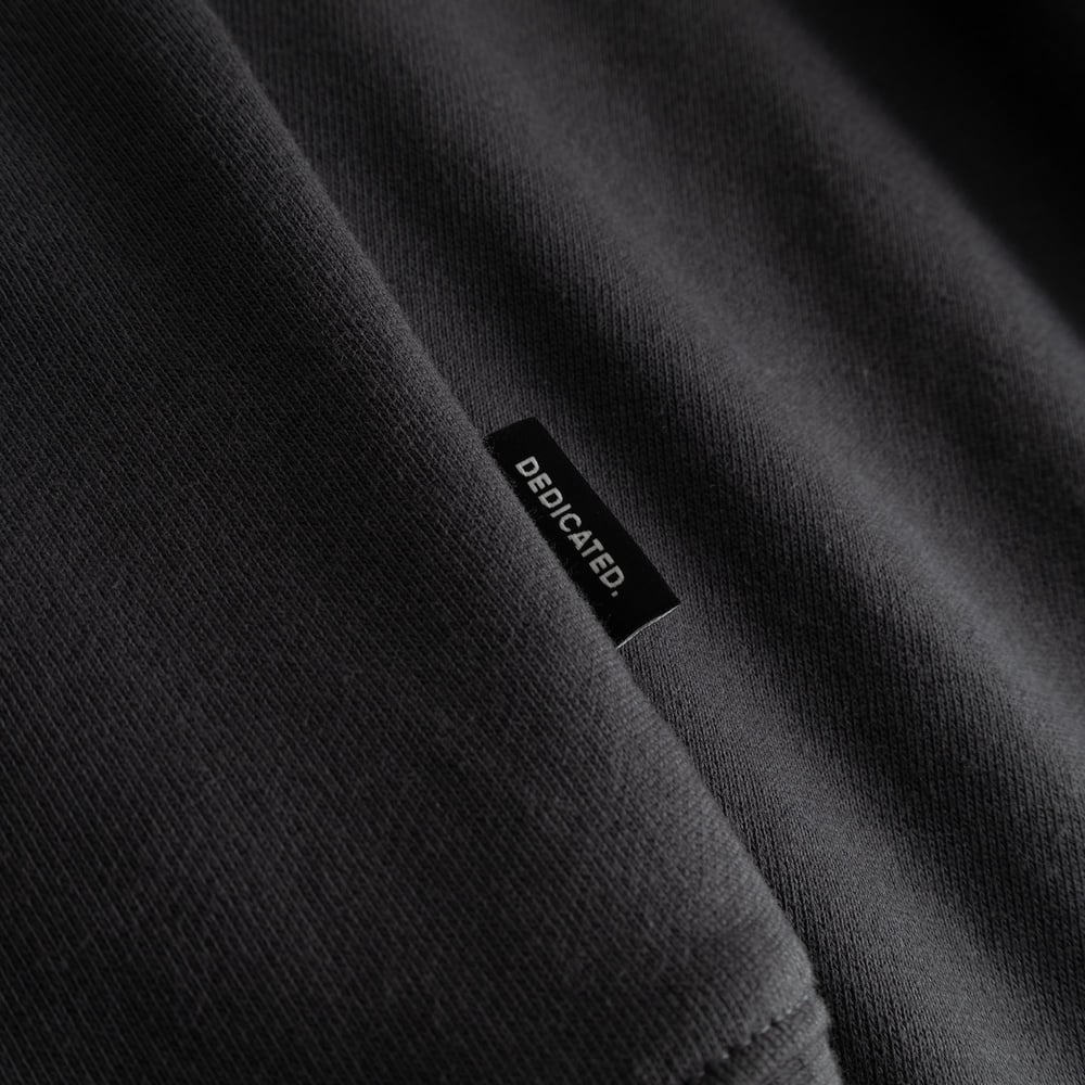 Close-up detail of the Dedicated brand label on the side of the charcoal Sweatshirt Malmoe Cheers Salud.