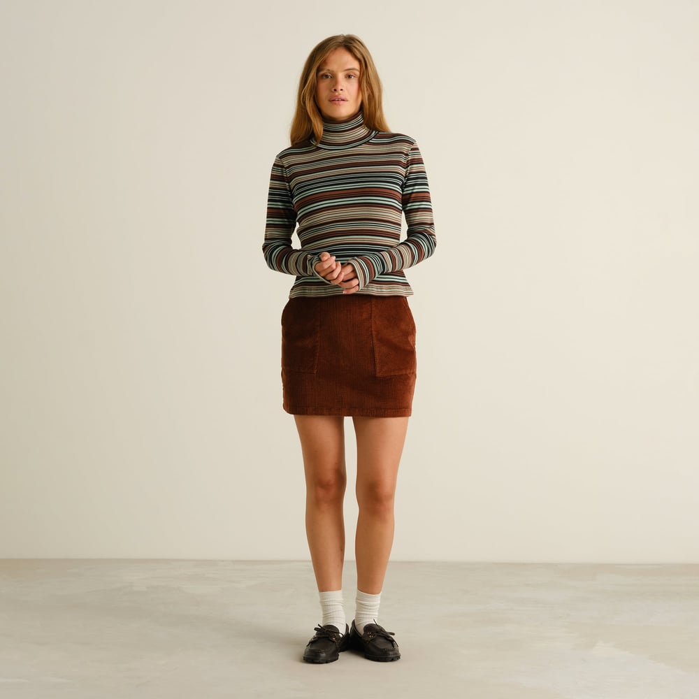 A model wears the Rib Top Malma in Irregular Stripe Green, styled with a brown corduroy skirt and black loafers.