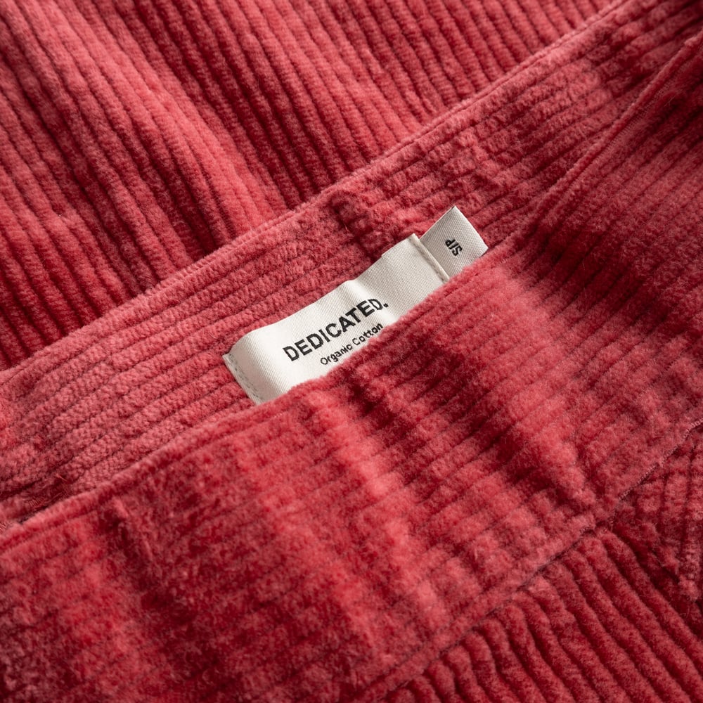 A detailed view of the rich Holly Red corduroy fabric of the Skirt Majorna, with the Dedicated brand label neatly tucked in.