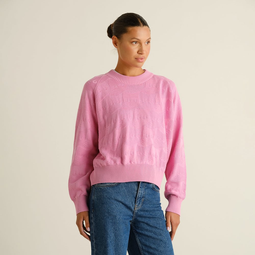 Model wears the boxy-fit Husie sweater in Moonlite Pink, featuring a textured cat pattern, styled with high-waisted jeans.