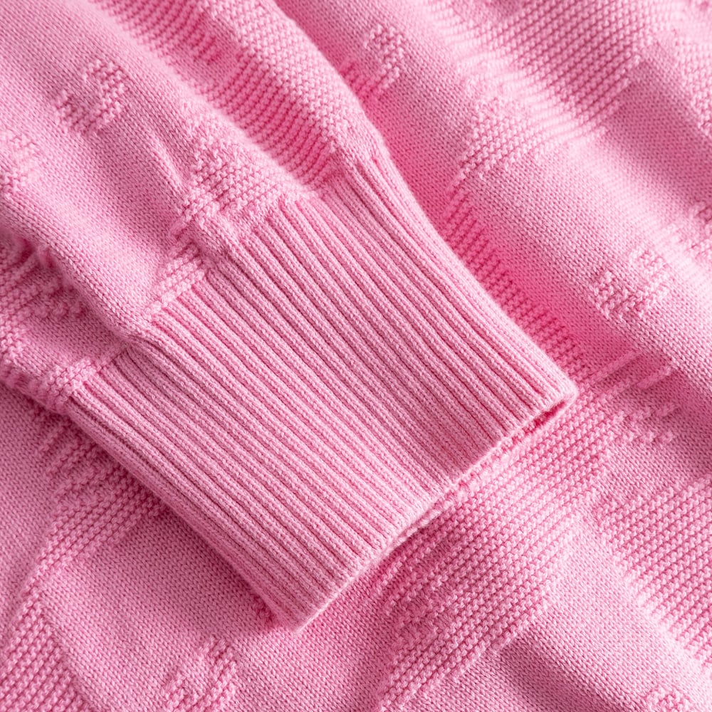 Close-up of the Husie sweater in Moonlite Pink, showing the ribbed cuff and the textured knit pattern with small cats.