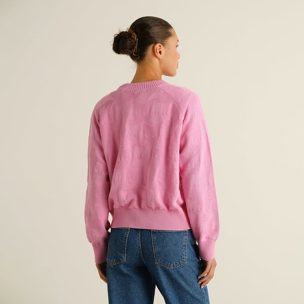 Woman seen from the back wearing the pink Husie Pepita Cats Knit sweater paired with blue jeans in a studio.