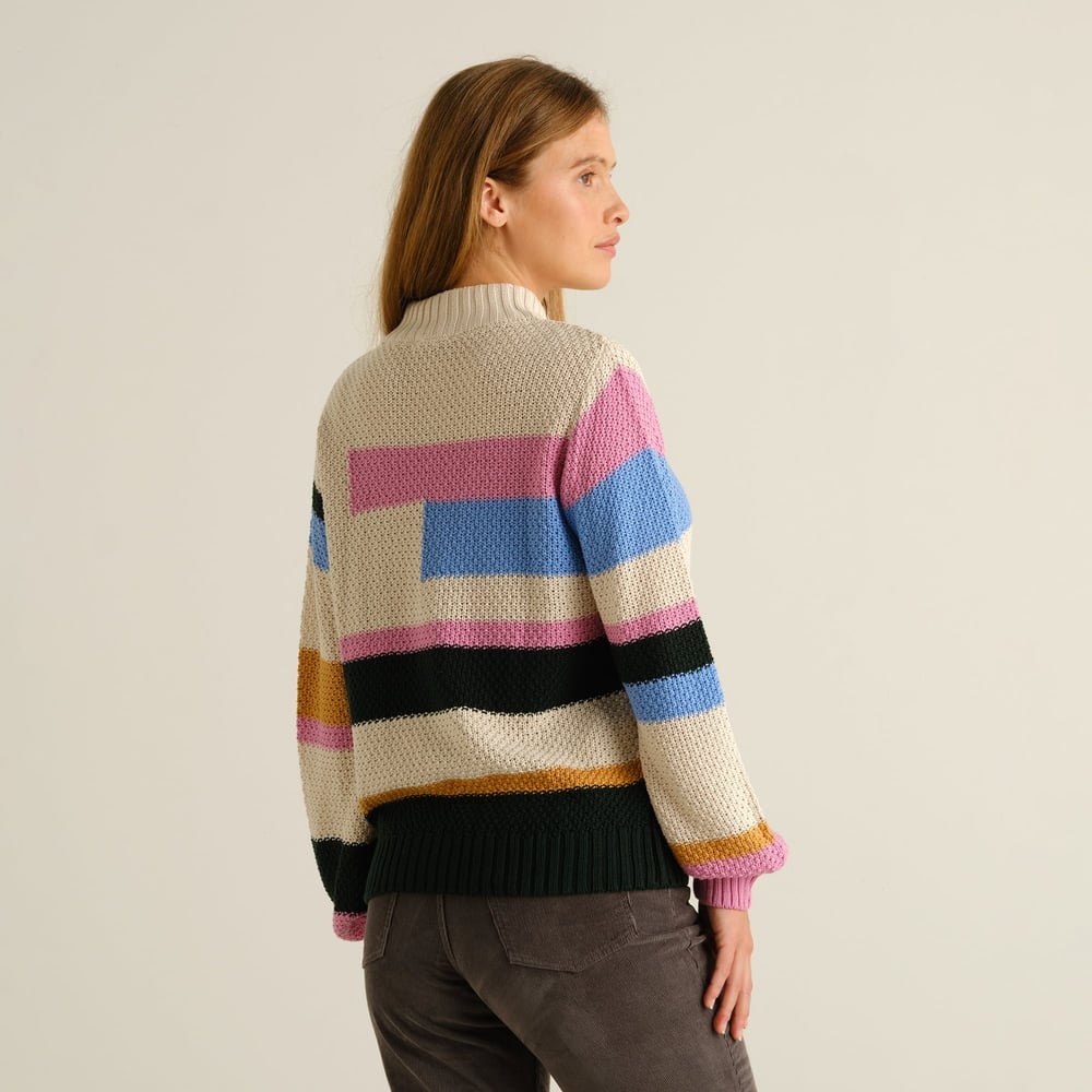 A woman looks over her shoulder, showing the back of the cozy, multi-colored Sweater Gotland Offset Stripe.