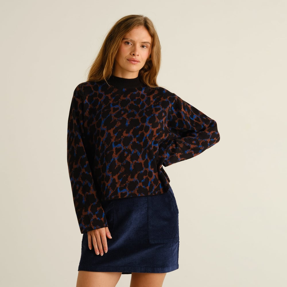 Front view of a model wearing the fun Sweater Limhamn with its multi-color leopard print and a dark blue corduroy skirt.